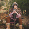Medieval reenactor woman in fur-trimmed clothing holding a longsword while sitting in a forest.
